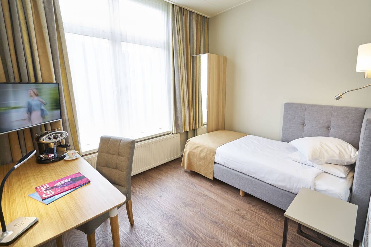 Ein Hotelzimmer mit einem Bett, einem Schreibtisch mit Computer, einem Sessel und einem Fernseher.