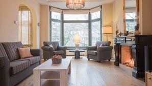 A living room with a fireplace, two armchairs, a sofa, a coffee table, and a chandelier.