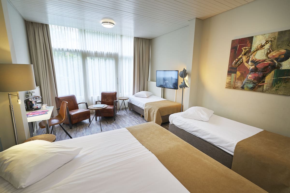 Ein Hotelzimmer mit zwei Betten, einem Schreibtisch, einem Stuhl, einem Fernseher und einem Bild an der Wand.