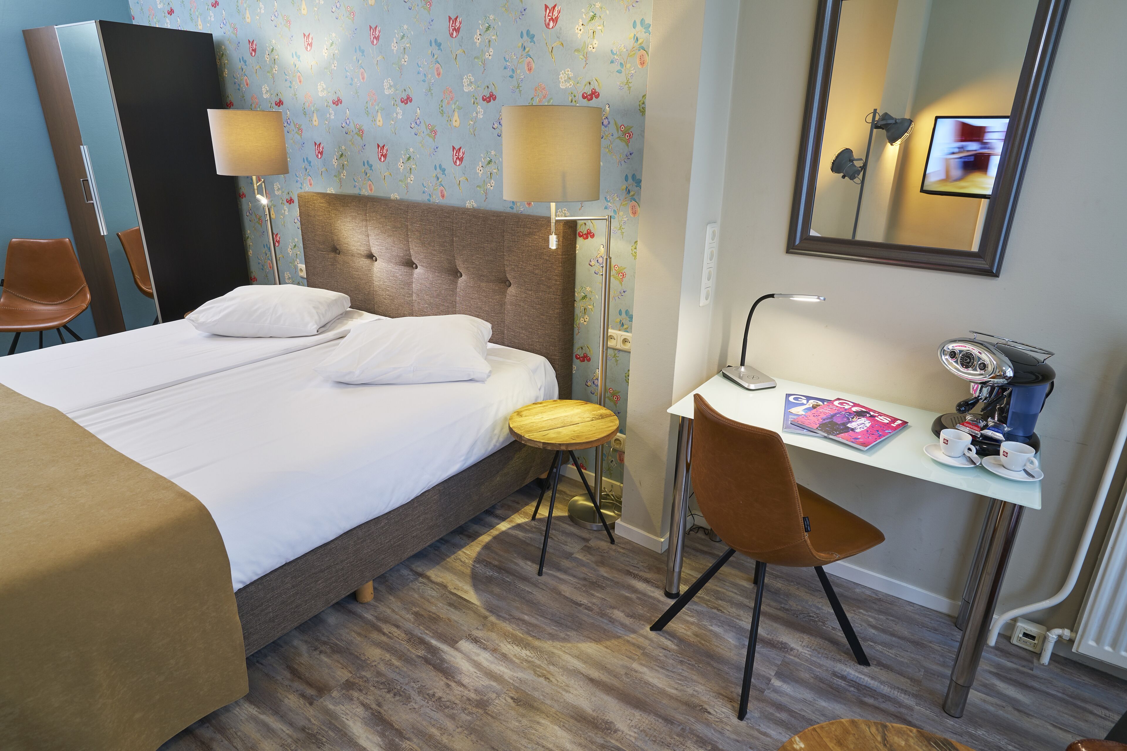 Quarto de hotel com cama, escrivaninha, cadeira, luminária e espelho.