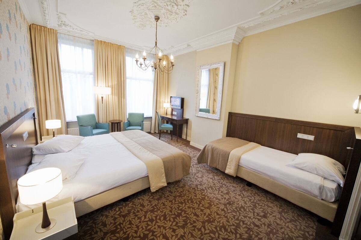 Ein Hotelzimmer mit zwei Betten, einem Schreibtisch, einem Fernseher, einem Sessel und einer Kandelaber.
