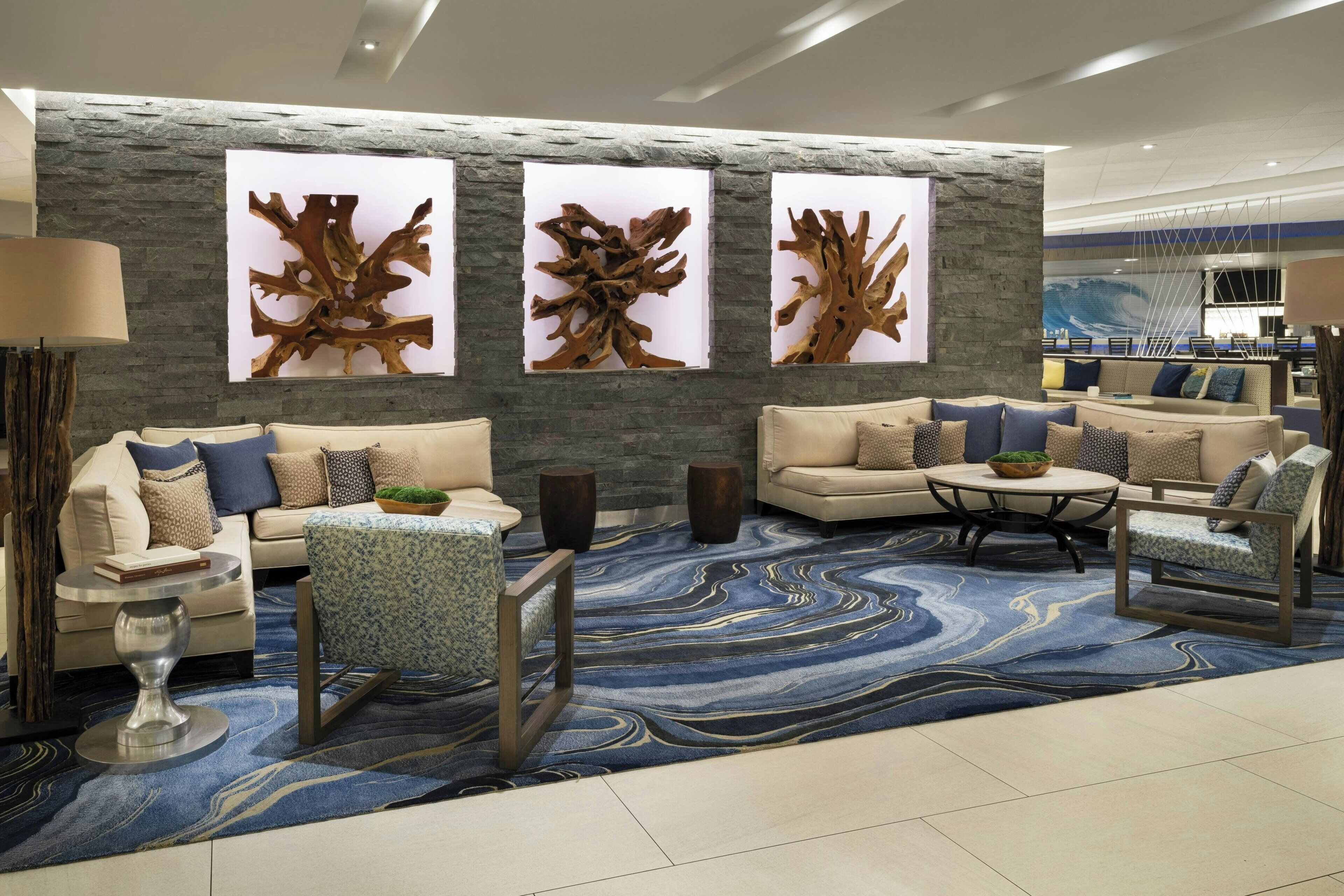 A modern living room with a stone accent wall, a blue marble rug, and a seating area with sofas and armchairs.