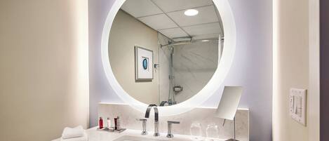A modern bathroom with a round mirror, a sink, and a shower.