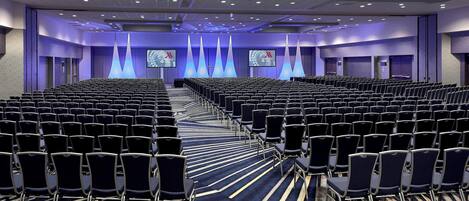 A conference room with rows of chairs, a carpeted floor, and a stage with screens.