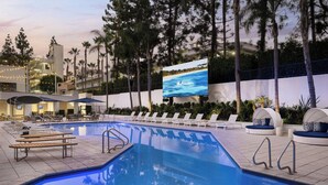 A swimming pool with lounge chairs and a large screen displaying a beach scene. - Irvine Marriott (Irvine)