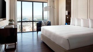 A hotel room with a large bed, a desk with a flat-screen TV, a chair, and a view of the city through large windows. - Irvine Marriott (Irvine)
