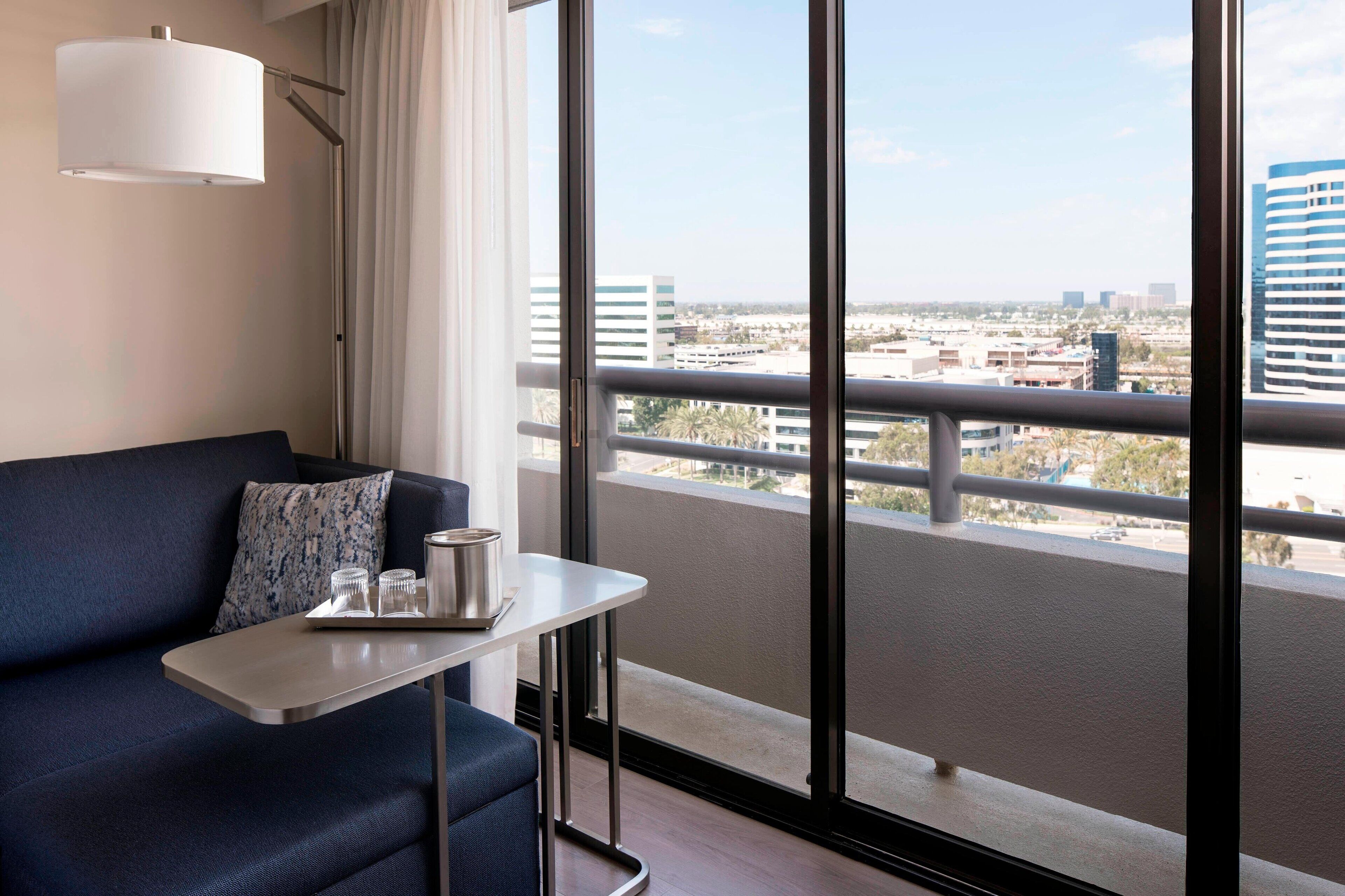 A modern hotel room with a balcony, a sofa, a small table, and a city view.