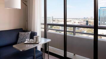 A modern hotel room with a balcony, a sofa, a small table, and a city view.