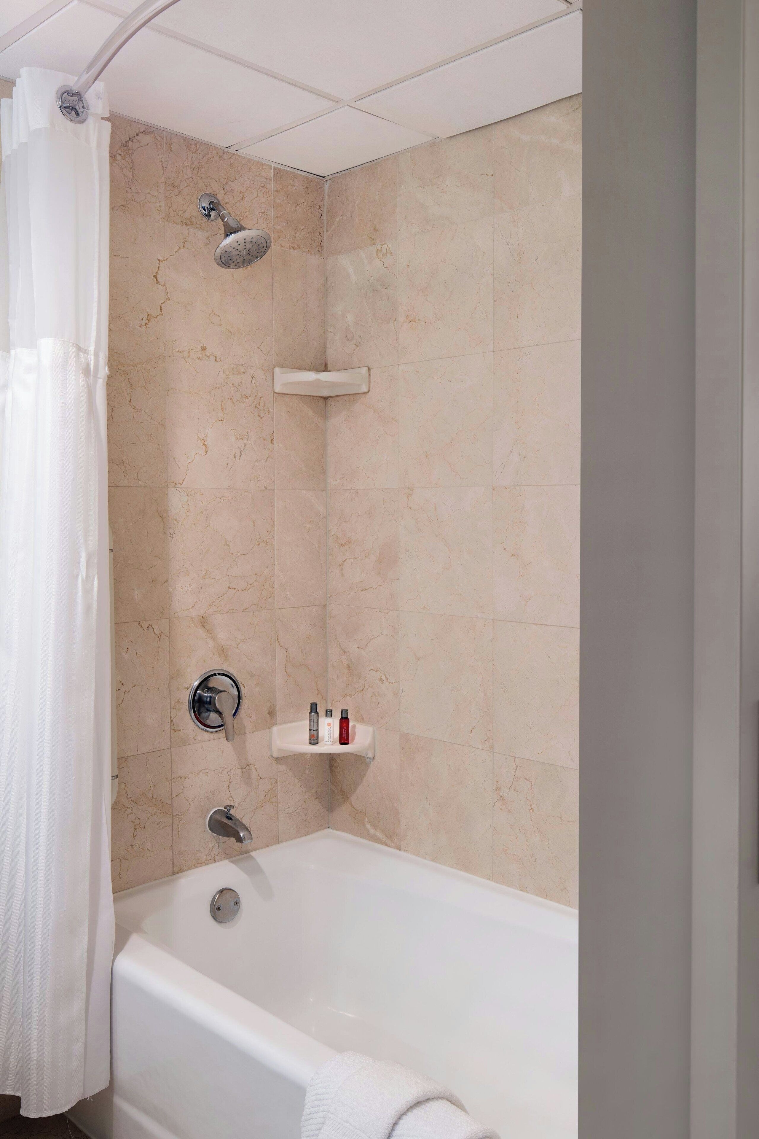 A modern bathroom with a bathtub, shower, and a shelf with toiletries.