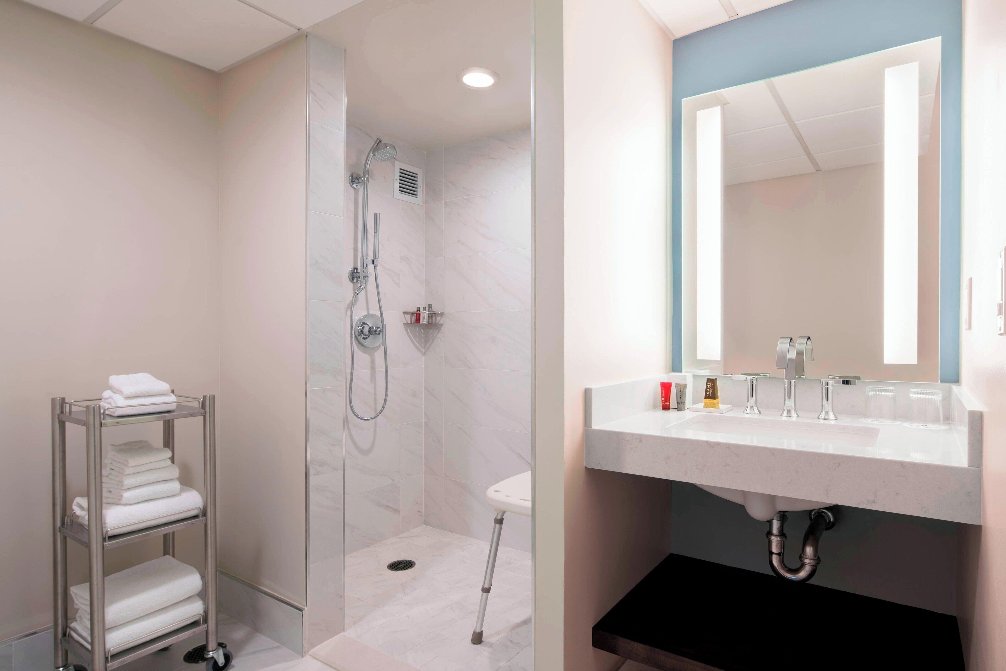 Un baño moderno con ducha a ras de suelo, un lavabo blanco con espejo y un toallero con toallas dobladas.