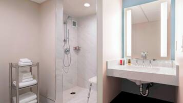 Un baño moderno con ducha a ras de suelo, un lavabo blanco con espejo y un toallero con toallas dobladas.