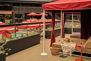 A rooftop terrace with red umbrellas, a pool, and a seating area with a hat and sunglasses. - Trailborn Jackson Hole, Outdoor Collection by Marriott Bonvoy (Jackson)