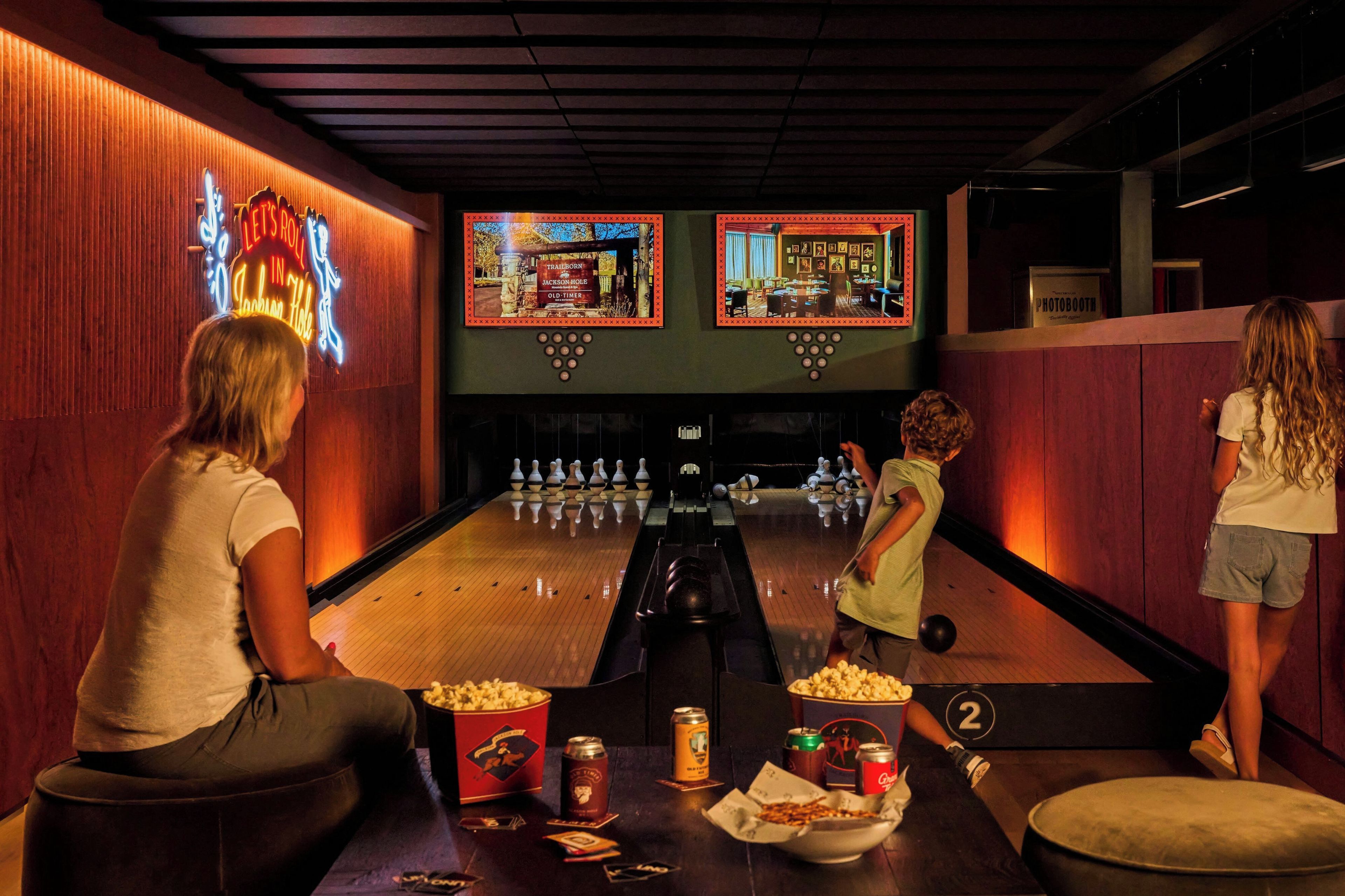 A bowling alley with pinsetters, a neon sign, and a photo booth.