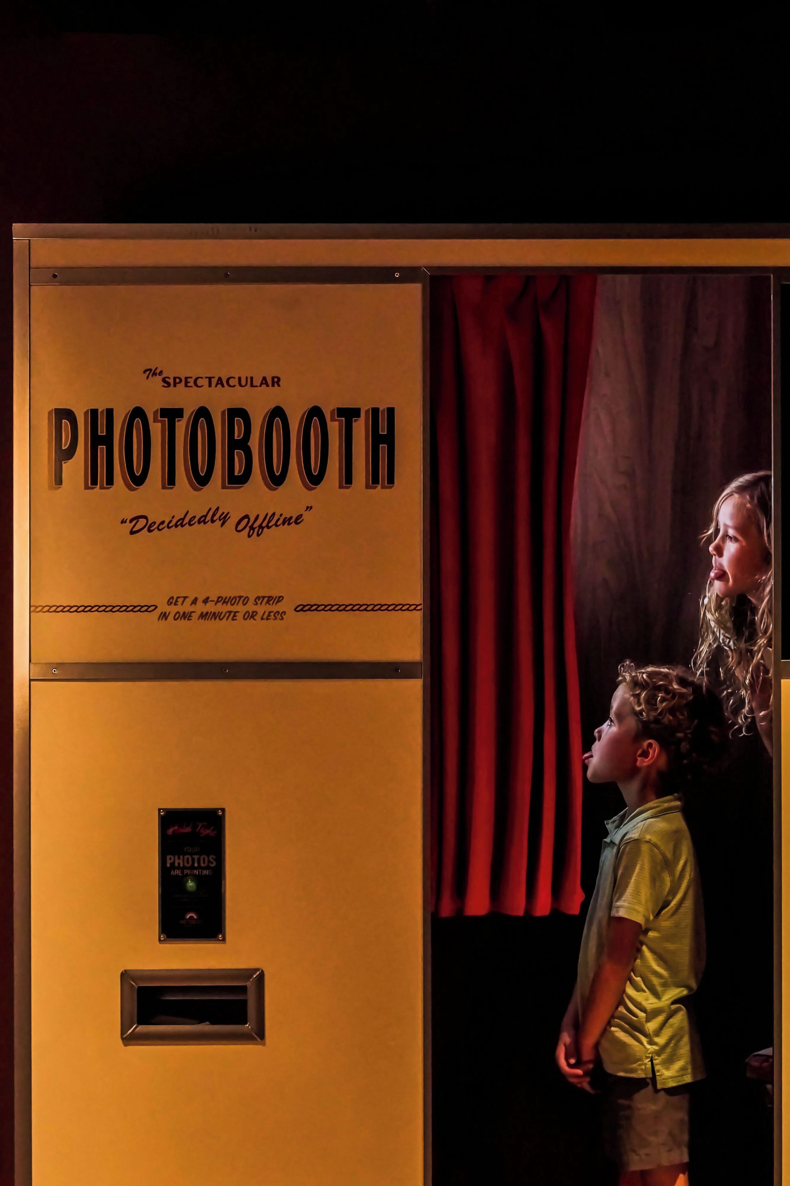 A vintage-style photo booth with a sign that reads 'The Spectacular PHOTOBOOTH 'Decidedly Offline''.
