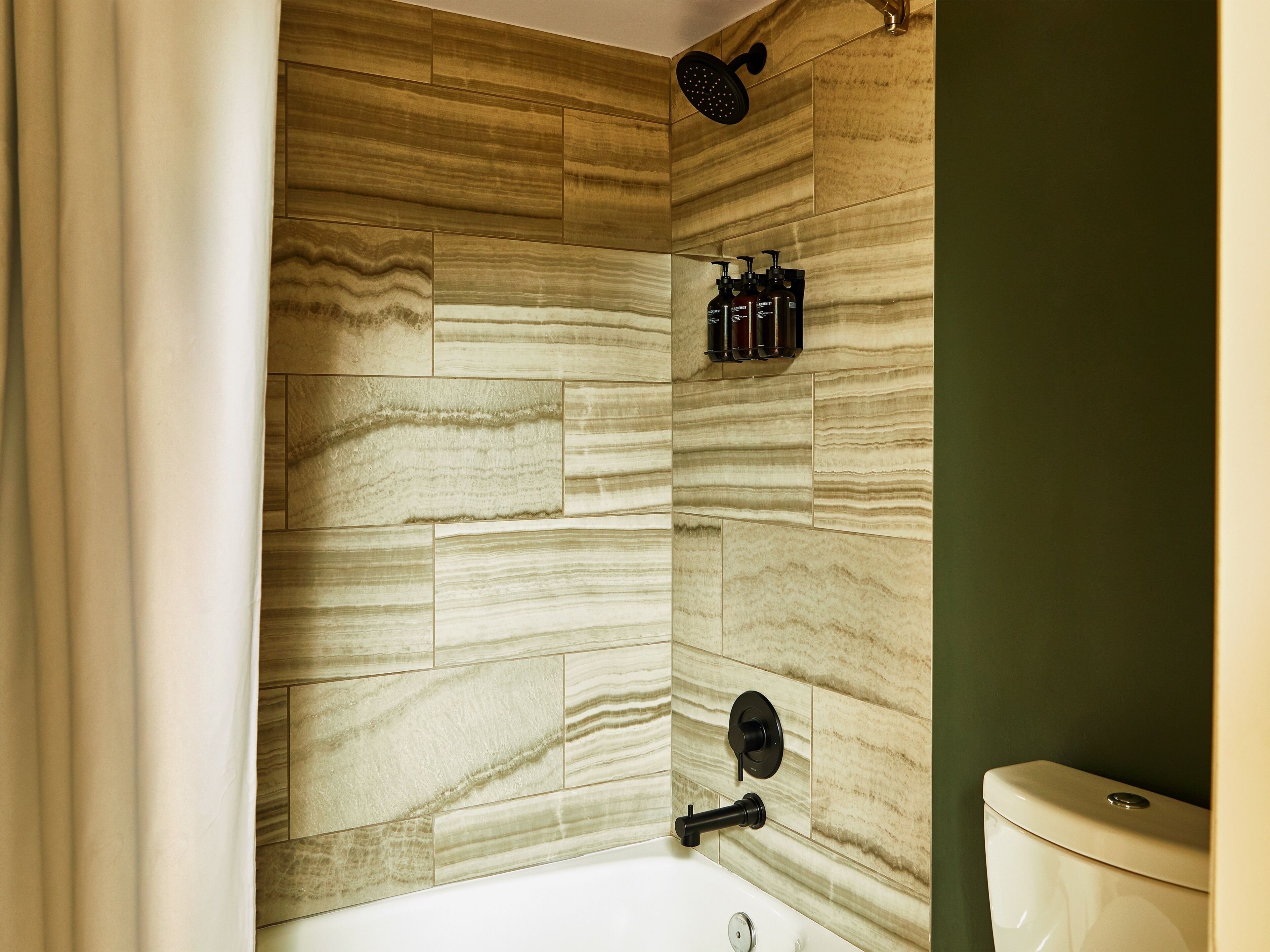 A bathroom with a shower, toilet, and a wall-mounted soap dispenser.