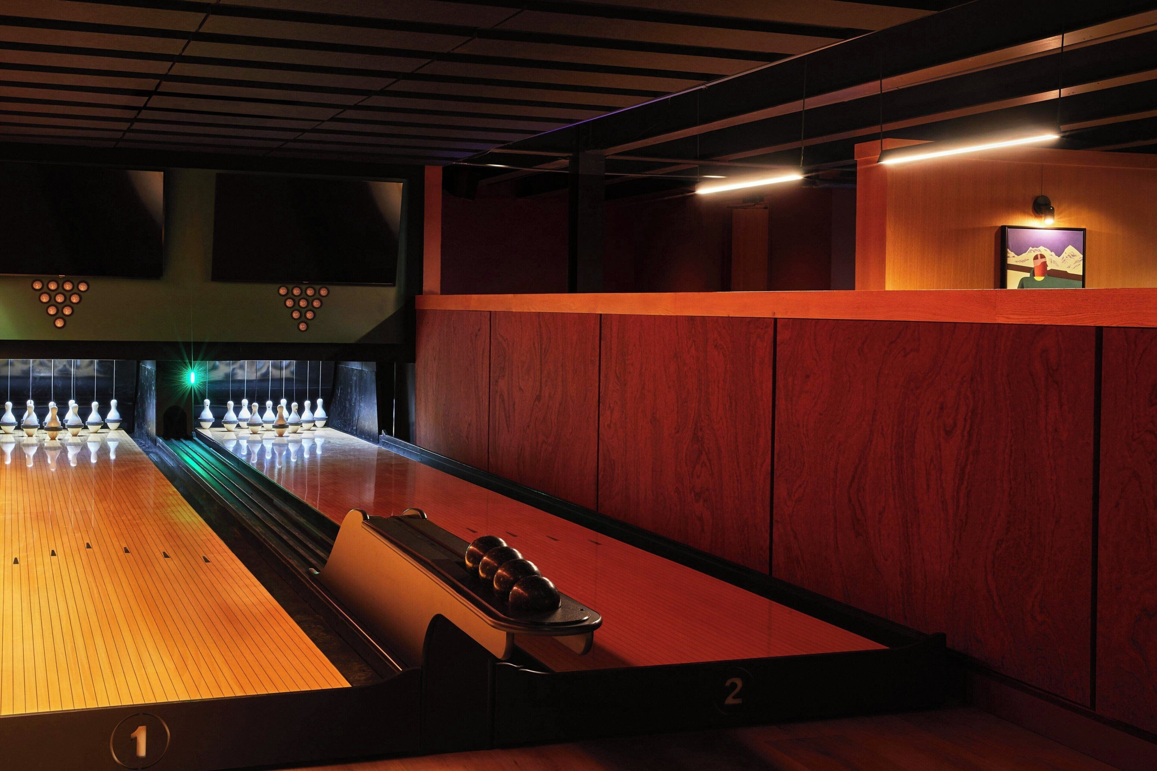A bowling alley with lanes, pins, and a bowling ball rack.