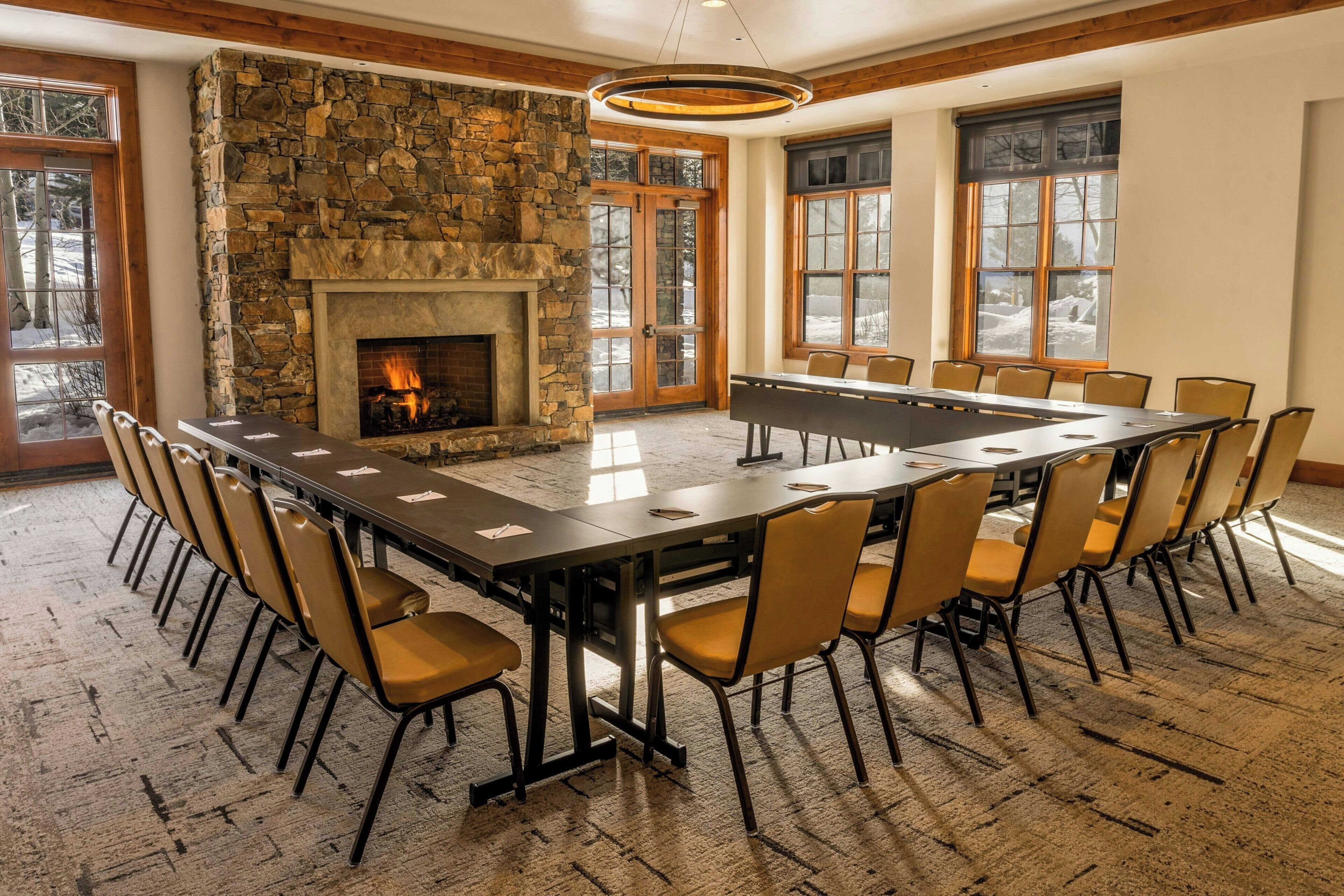 A conference room with a stone fireplace, large windows, and a long table with chairs.