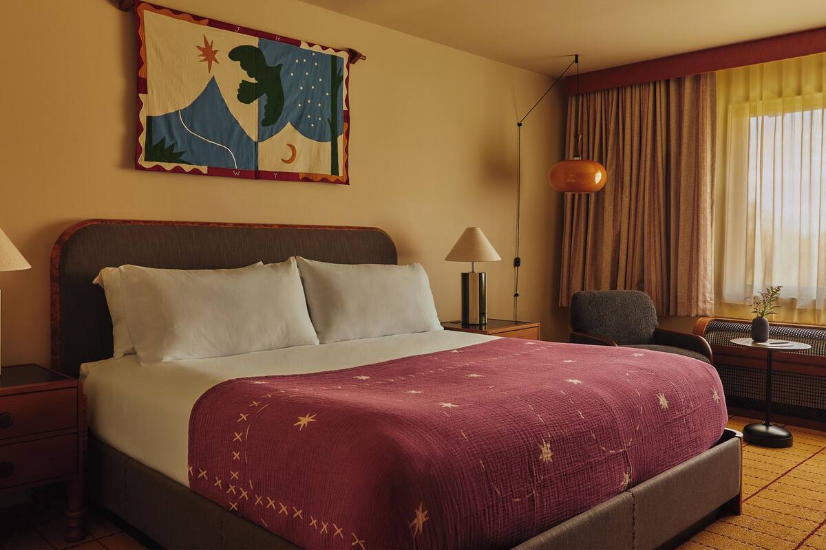 A hotel room with a bed, a nightstand, a lamp, a chair, and a window with curtains.