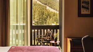 A room with a bed, a chair, a small table, and a view of a forested hillside.