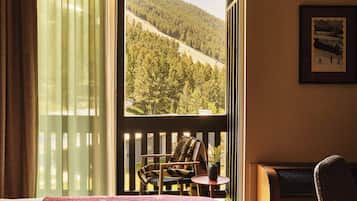 A room with a bed, a chair, a small table, and a view of a forested hillside.