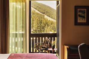 A room with a bed, a chair, a small table, and a view of a forested hillside.