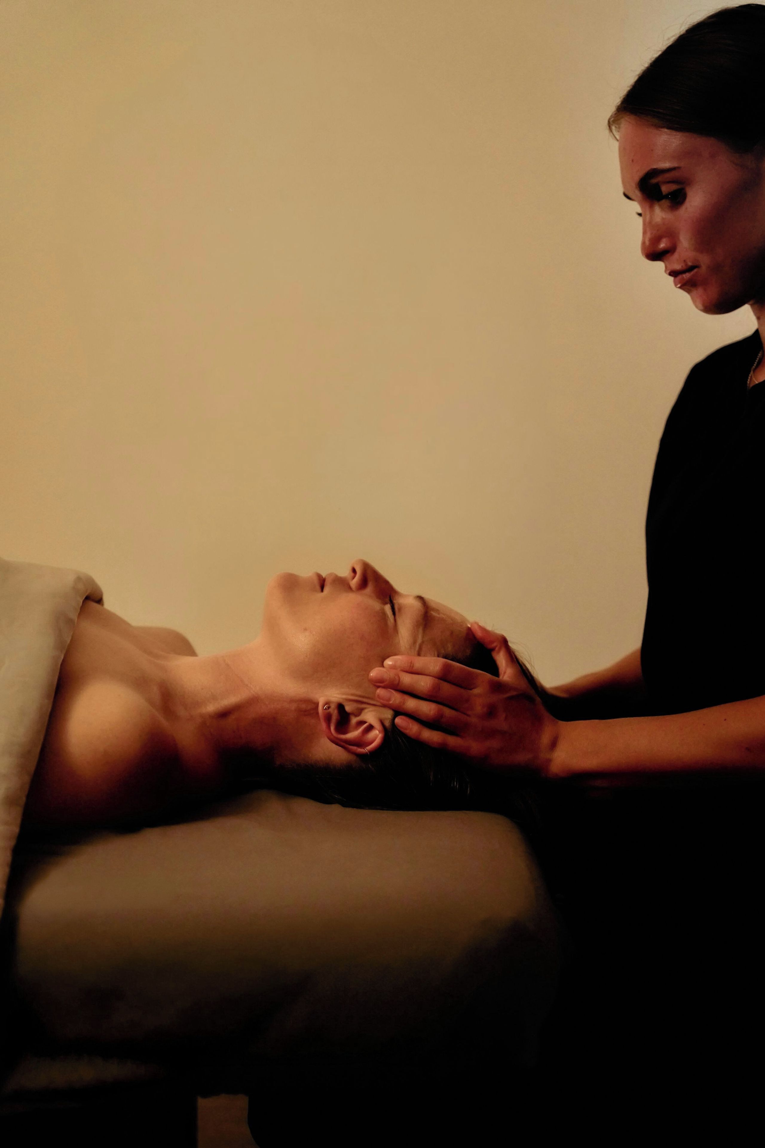 A person lying on a massage table receiving a head massage.