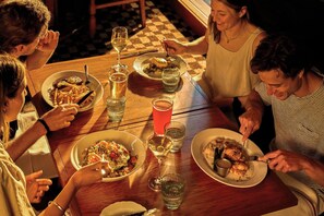 A group of people dining at a wooden table with various dishes, glasses of beverages, and cutlery.