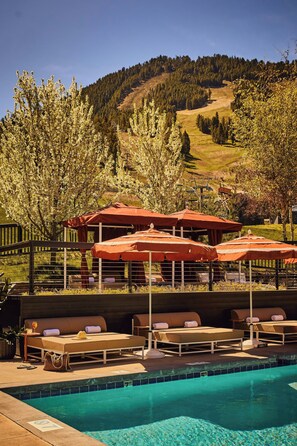 A poolside area with lounge chairs and umbrellas, a clear blue pool, and a mountainous backdrop.