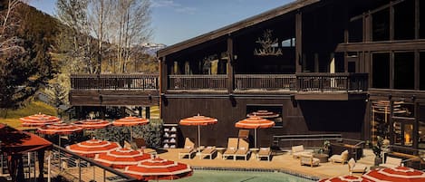 A poolside area with sun loungers and umbrellas, a wooden building with balconies, and a mountainous backdrop.