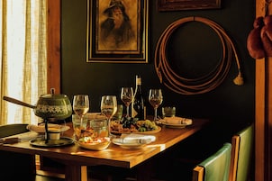 Mesa de jantar posta com copos de vinho, uma garrafa e diversas opções de comida.