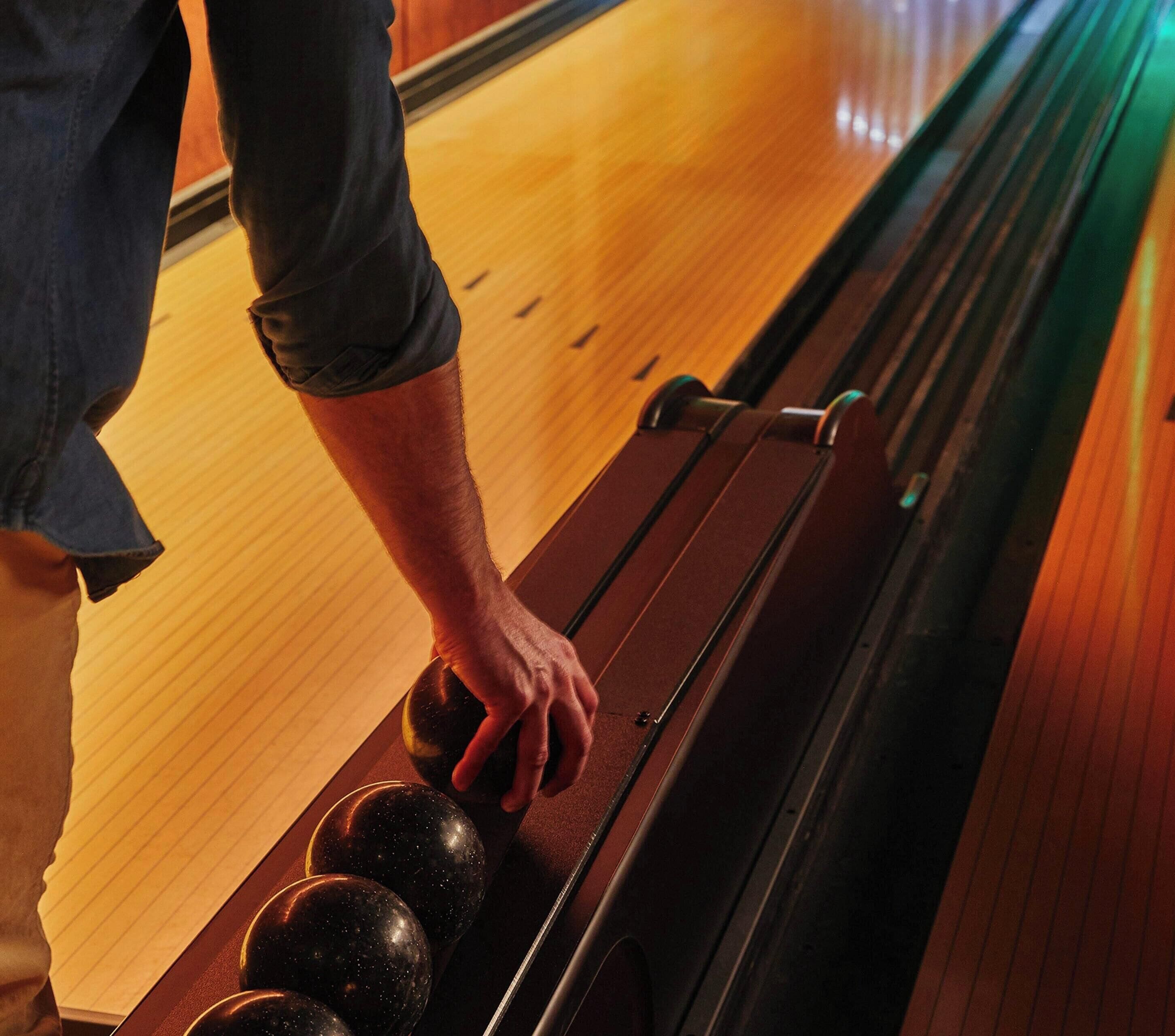 Een hand plaatst een bowlingbal op de baan.