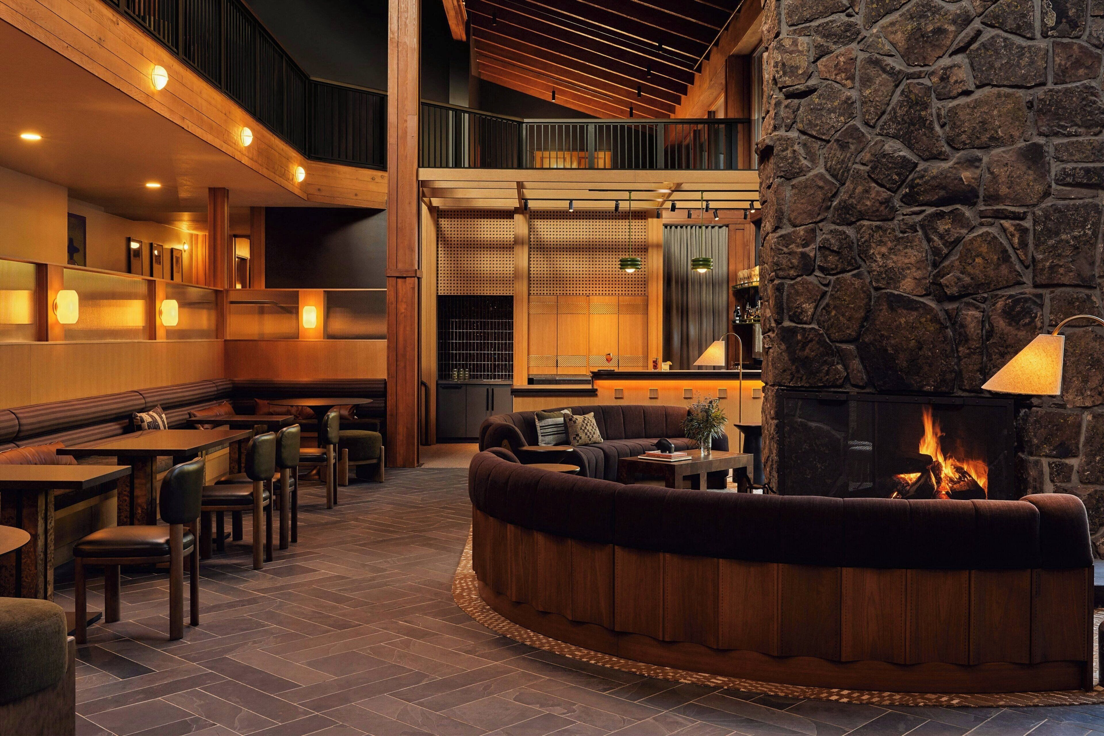 A restaurant with a stone fireplace, wooden seating, and a high ceiling.