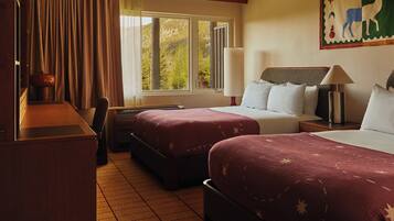 A hotel room with two beds, a desk, a chair, a lamp, and a window with a view of trees.