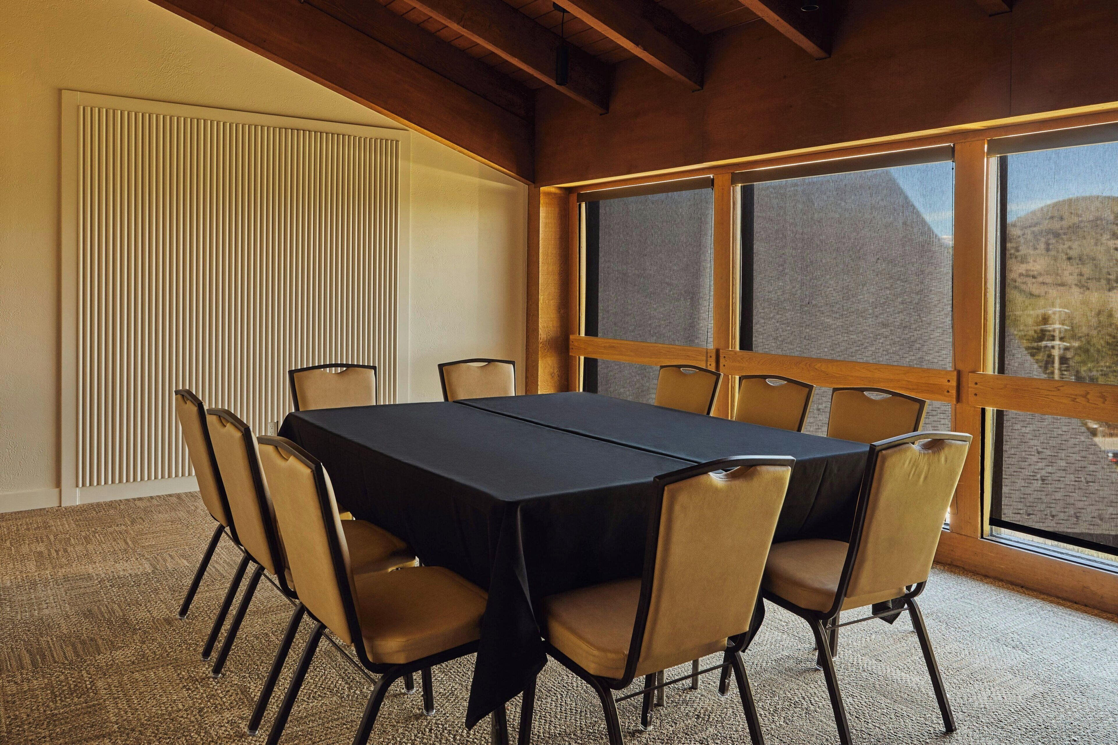 A conference room with a large table and chairs, large windows, and a wooden ceiling.
