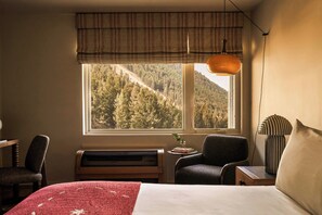 A bedroom with a large window, a bed, a chair, a table, and a radiator.