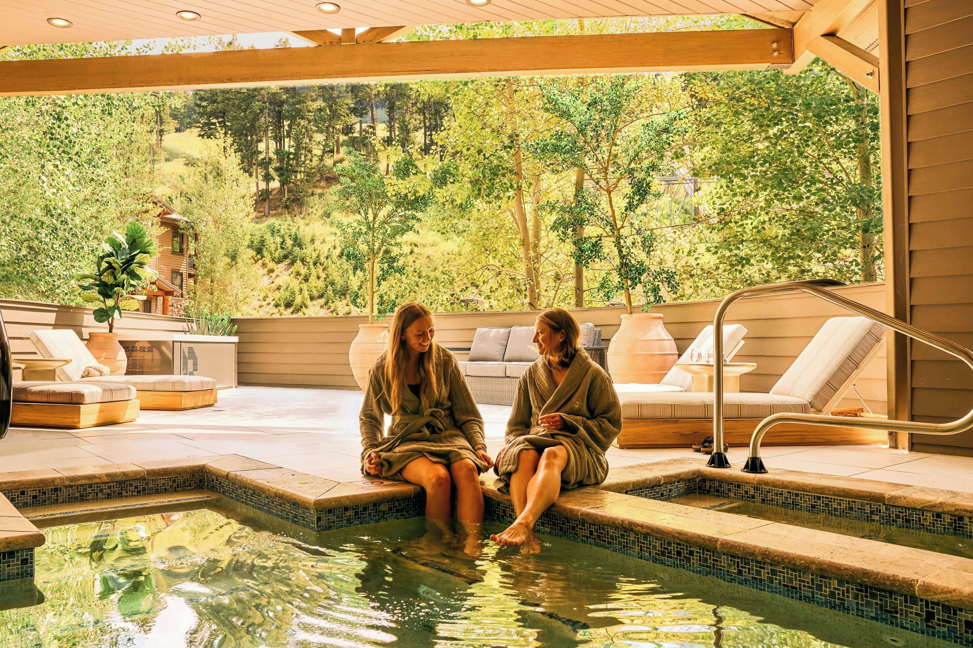 Two individuals seated by a pool with a view of a forested landscape.