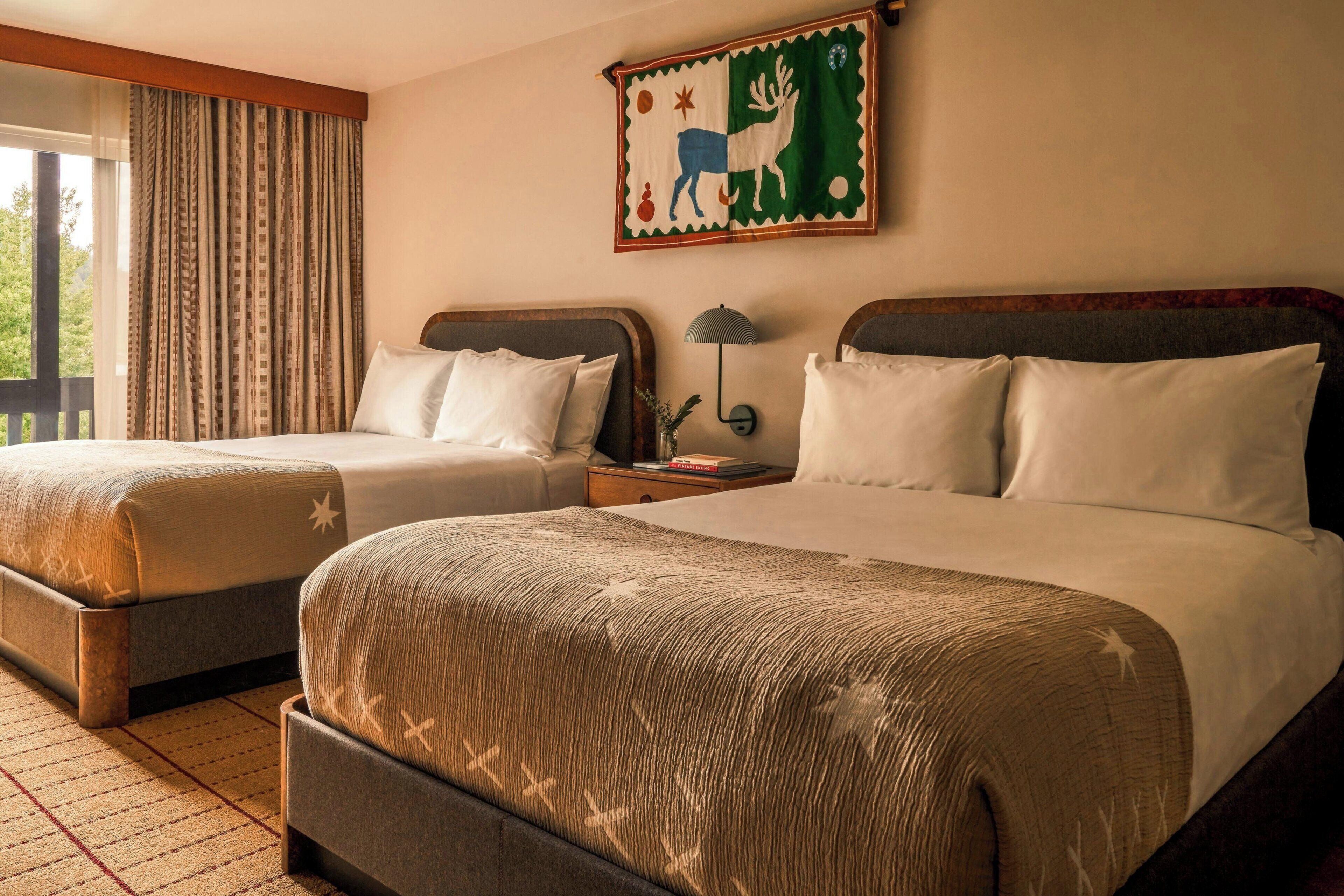 A hotel room with two beds, a nightstand, a lamp, and a painting on the wall.