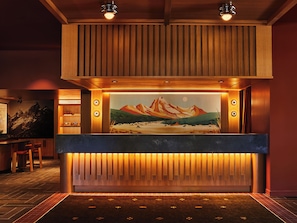 A reception area with a wooden reception desk, a mural of mountains, and a herringbone-patterned floor. - Trailborn Jackson Hole (Jackson)