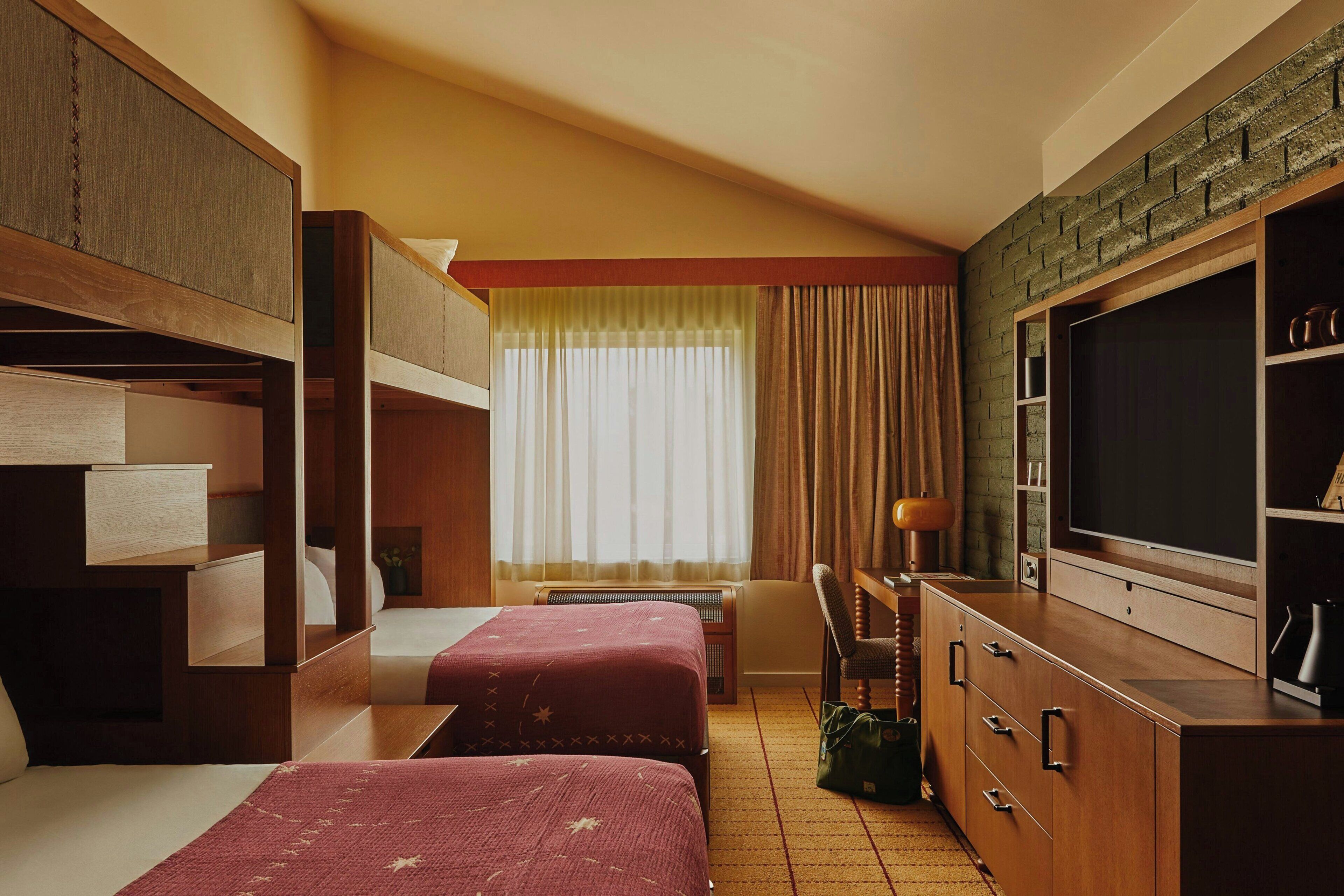 Een hotelkamer met stapelbedden, een televisie, een bureau en een raam met gordijnen.
