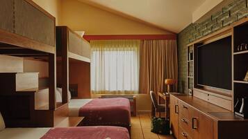 Een hotelkamer met stapelbedden, een televisie, een bureau en een raam met gordijnen.
