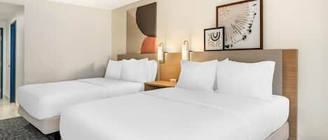 A hotel room with two single beds, a wooden headboard, a nightstand with a lamp, and a wall with abstract art.