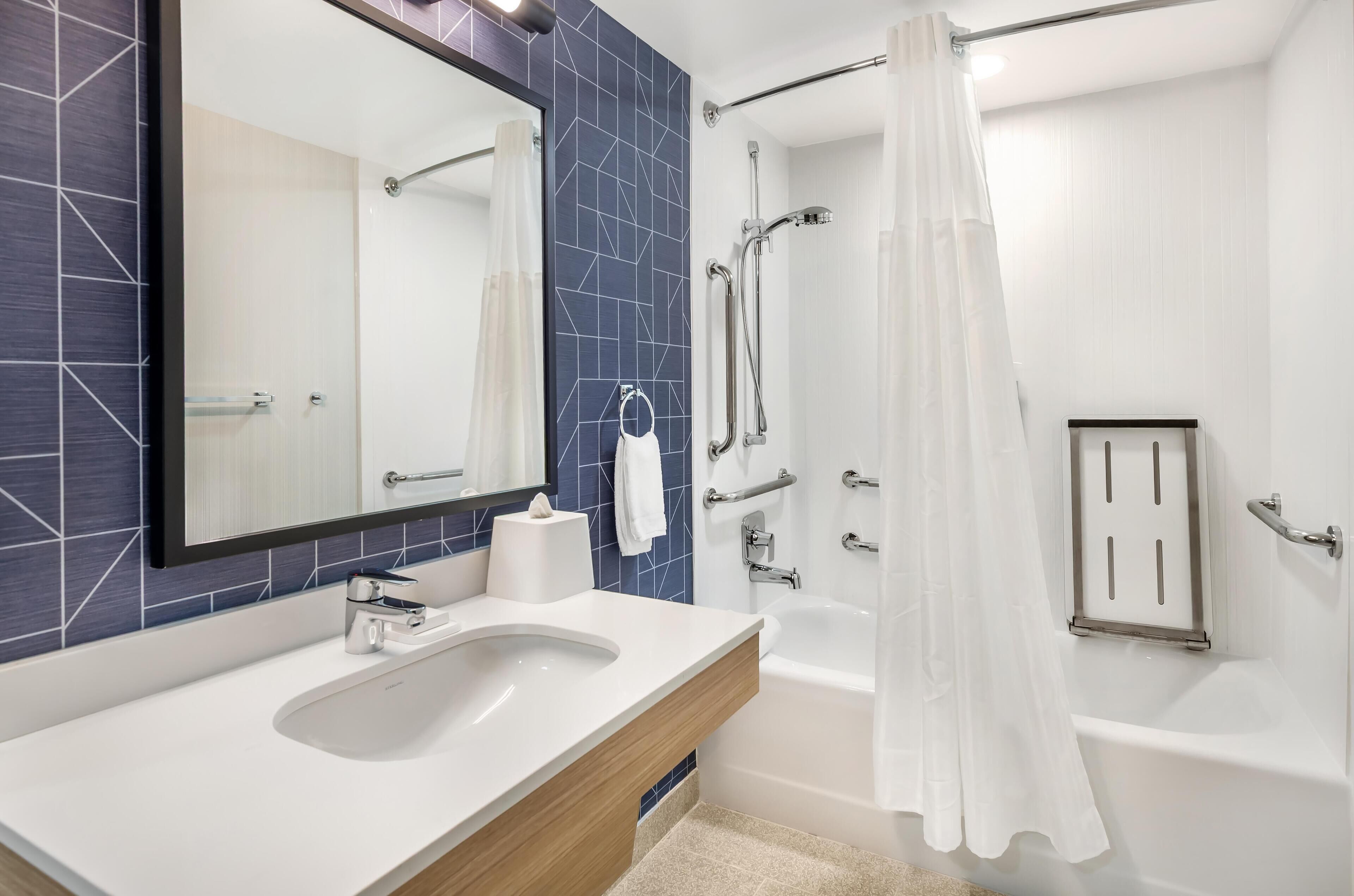 A modern bathroom with a white sink, a mirror, a shower with a glass door, and a towel rack.