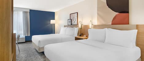 A hotel room with two beds, a large abstract painting, a desk with a lamp, and a window with curtains.