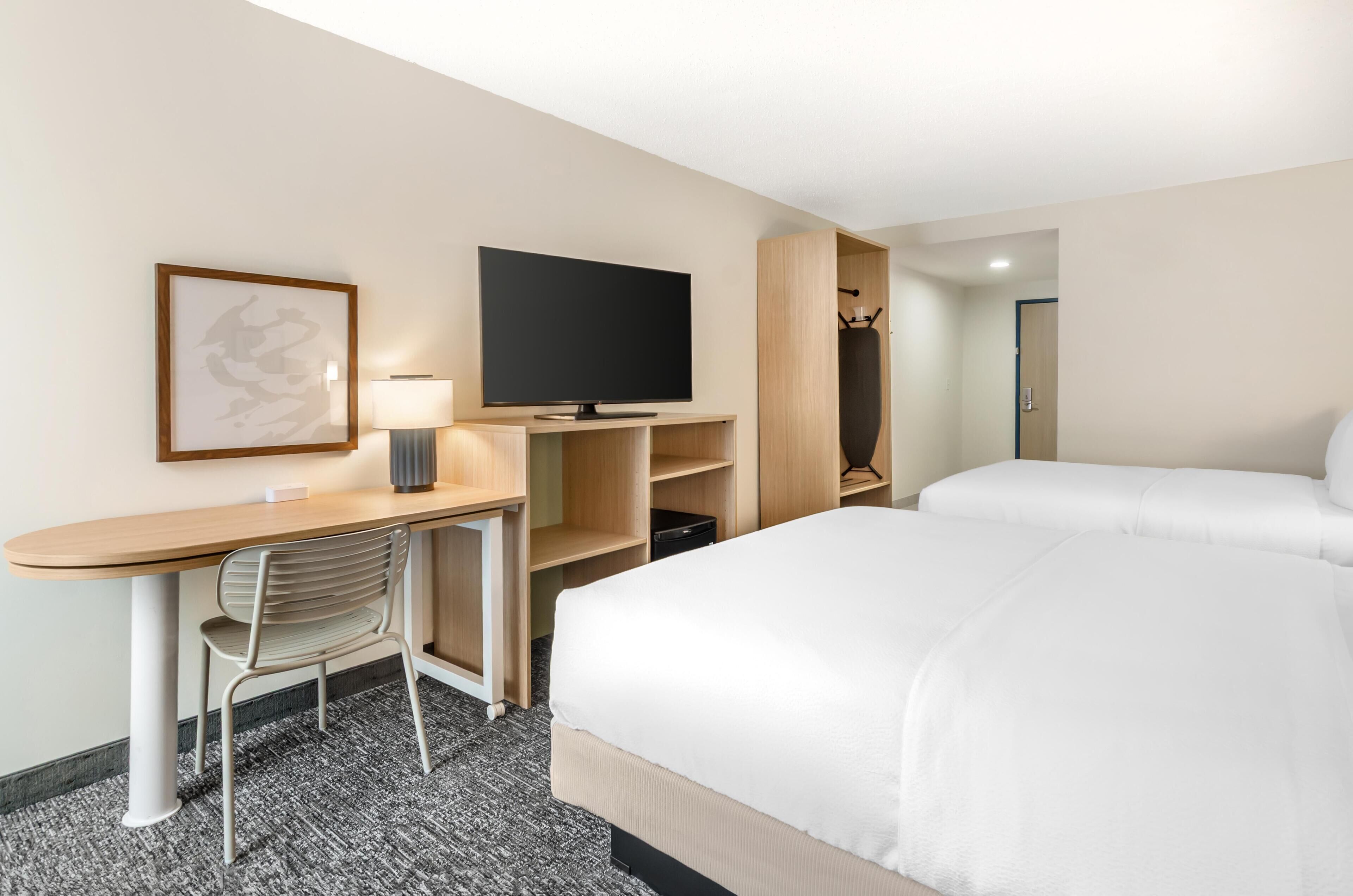 A hotel room with a bed, a desk with a chair, a television, and a wardrobe.