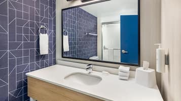 A modern bathroom with a large mirror, white sink, and towel rack.