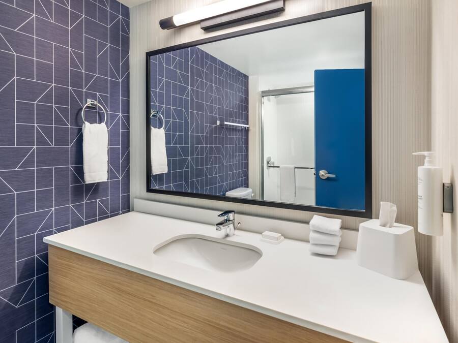 A modern bathroom with a large mirror, white sink, and towel rack.