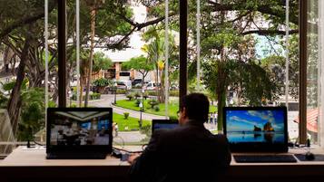 A man working at a desk with two laptops, overlooking a street with trees and buildings.