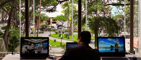 Un hombre trabaja en un escritorio con dos portátiles, con vistas a una calle con árboles y edificios.