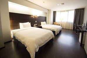 A hotel room with two beds, a desk, a chair, and a window with curtains. - Unipark by Oro Verde Hotels (Guayaquil)