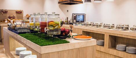 Una mesa de buffet con diferentes alimentos, una máquina de café y una pantalla de televisión.